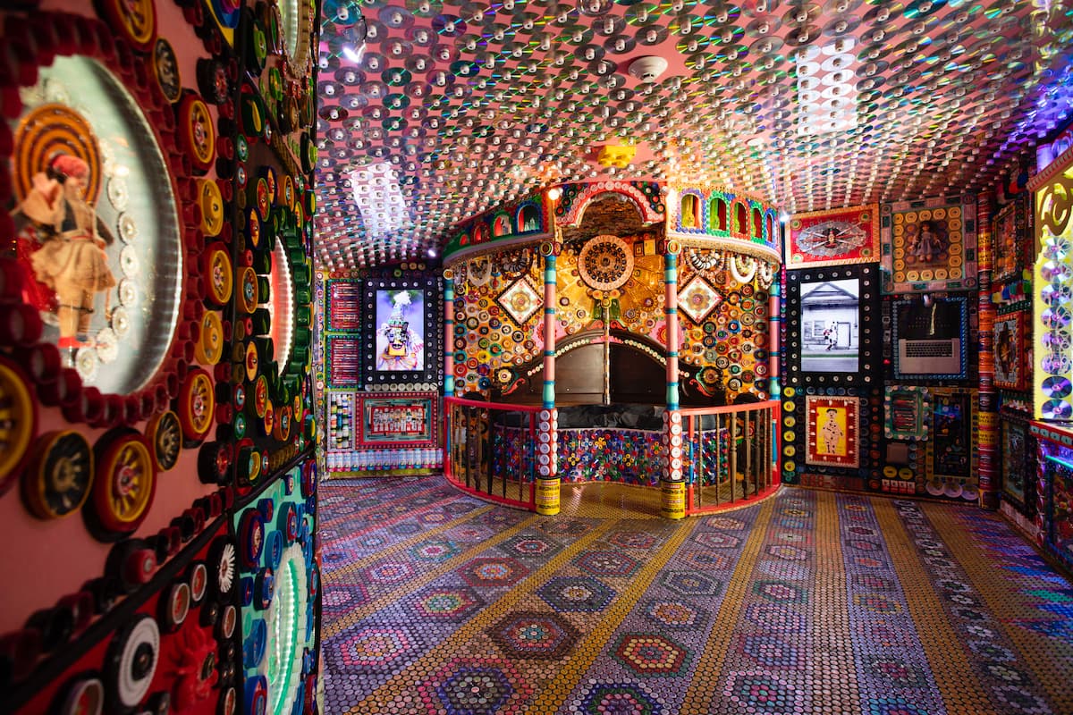 room with lots of CDs on the ceiling, tiles on the floor in geometric shapes, and a small room against the wall with designs on it and colorful spindles