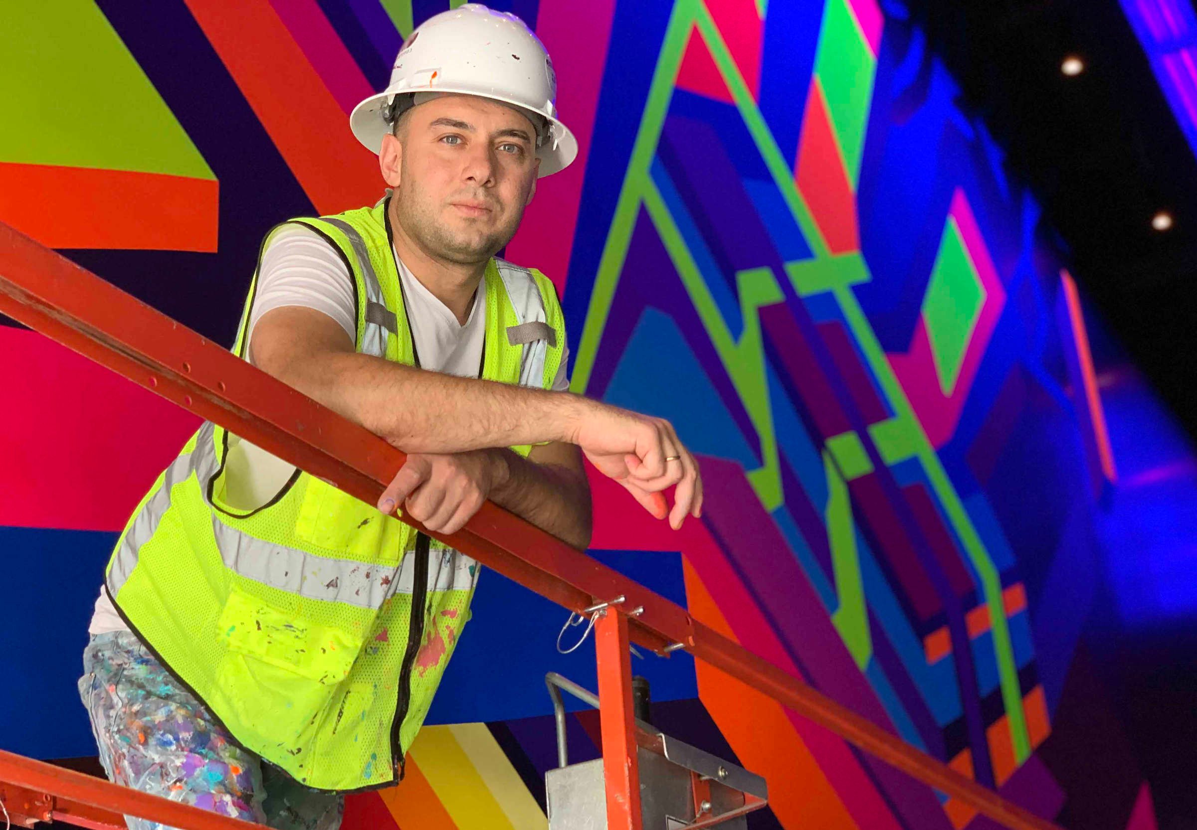 The artist poses in front of his colorful and geometric mural.